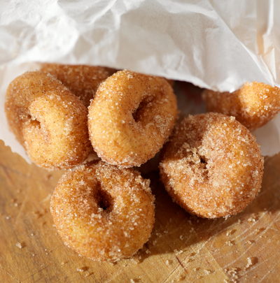 Candy donuts coated in sugar, piled on a wooden surface with white paper in the background.